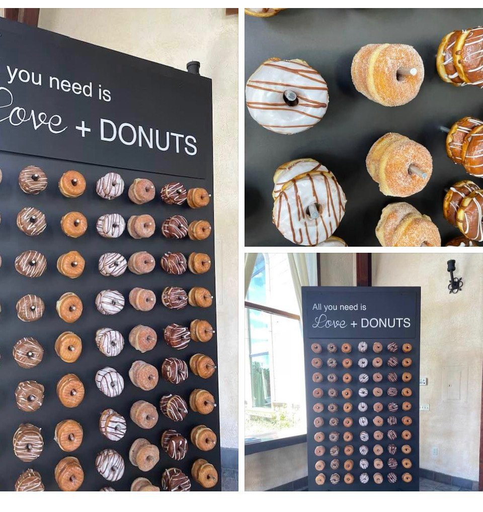 A donut wall built by The Donut Run at a Utah event — a freestanding black board reading All you need is Love and Donuts, hung with rows of ring donuts on pegs